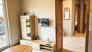 A room with a wooden cabinet, a television mounted on the wall, and a wooden door leading to another room. - Beautiful apartment for 4 guests with WIFI, TV and terrace (Trassenheide)