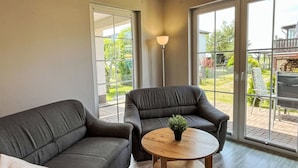 A modern living room with a grey sofa, a round wooden coffee table with a plant, and large sliding glass doors leading to an outdoor patio area. - Beautiful apartment for 4 guests with WIFI, TV and terrace (Trassenheide)
