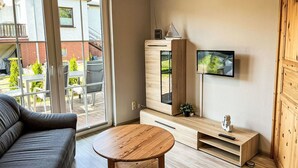 A modern living room with a sofa, a wooden coffee table, a TV mounted on the wall, and a sliding glass door leading to an outdoor area. - Beautiful apartment for 4 guests with WIFI, TV and terrace (Trassenheide)