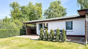 A single-story house with a covered porch, a small deck, and a well-maintained lawn. - Cosy apartment for 3 people with WIFI, TV and terrace (Trassenheide)