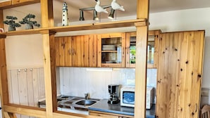 A compact kitchen with wooden cabinets, a sink, a stove, and a microwave. - Cosy apartment for 3 people with WIFI, TV and terrace (Trassenheide)