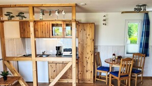 A compact kitchen with wooden cabinetry, a coffee maker, and a toaster. There are two wooden chairs with blue cushions around a small round table. - Cosy apartment for 3 people with WIFI, TV and terrace (Trassenheide)
