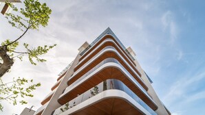 Un moderno edificio de varios pisos con un diseño arquitectónico curvo y distintivo, que presenta balcones con barandillas de madera.