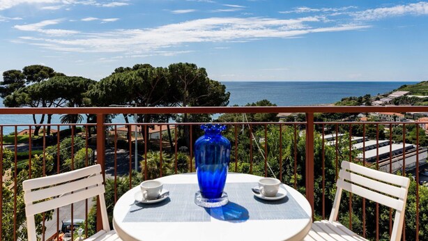 A round table with two white chairs, a blue vase, and two white cups on a balcony overlooking a coastal view with trees and buildings. - Cosy apartment for 6 guests with WIFI, A/C, TV, balcony and pets allowed (Sanremo)