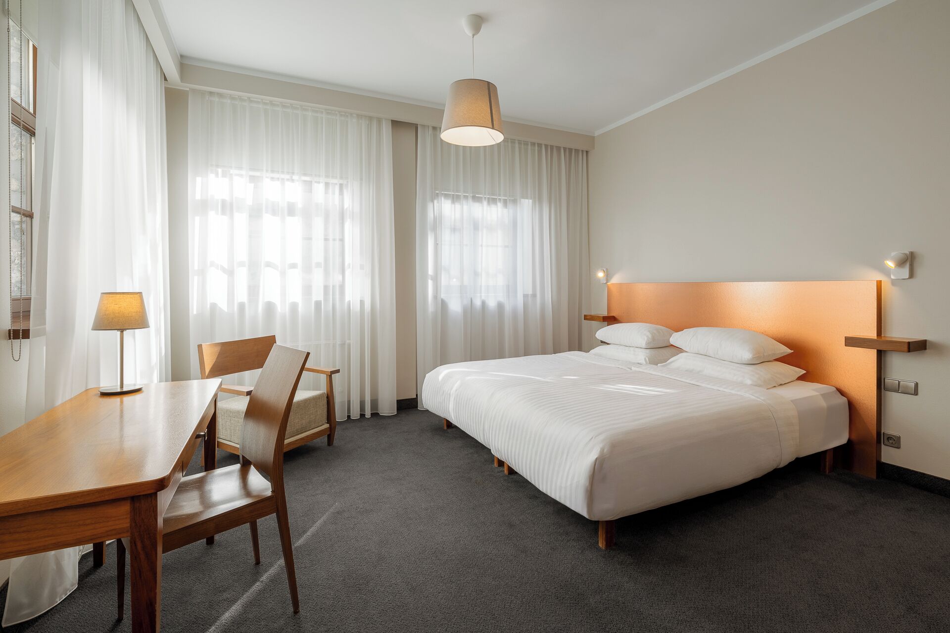A hotel room with a bed, a desk, a chair, and a lamp.