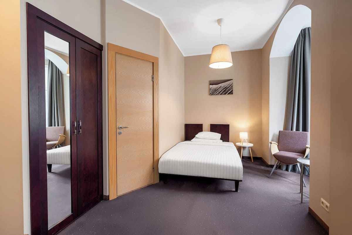 Una habitación de hotel con cama, mesitas de noche, una silla, armario y lámpara en el techo.