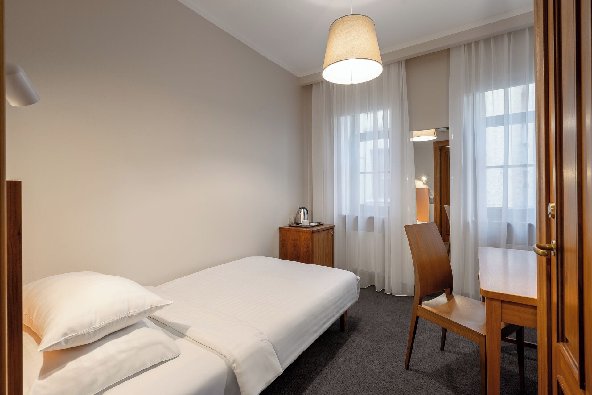 Hotellihuone, jossa on sänky, puinen yöpöytä, tuoli ja työpöytä.