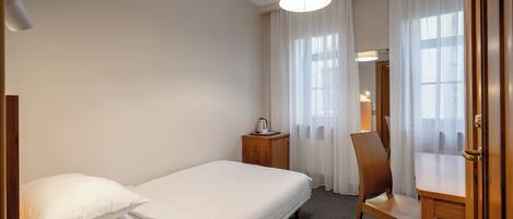 A hotel room with a bed, a wooden nightstand, a chair, and a desk.