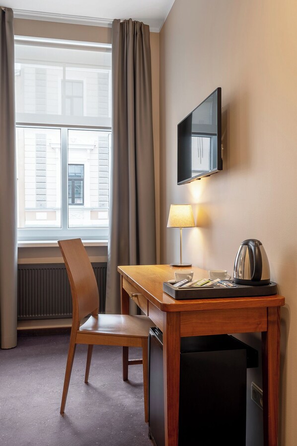 A hotel room with a wooden desk, a chair, a television mounted on the wall, a lamp, and a kettle on a table. - RIJA Riga City Center Hotel (Riga)