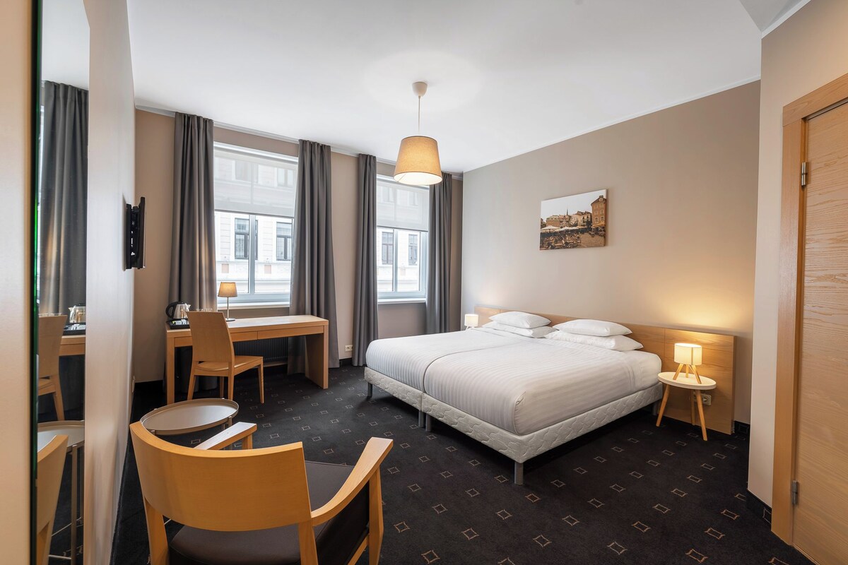 Habitación de hotel con cama, escritorio, silla y ventana con cortinas.