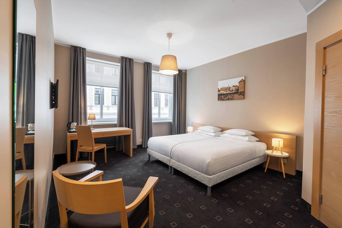Habitación de hotel con cama, escritorio, silla y ventana con cortinas.
