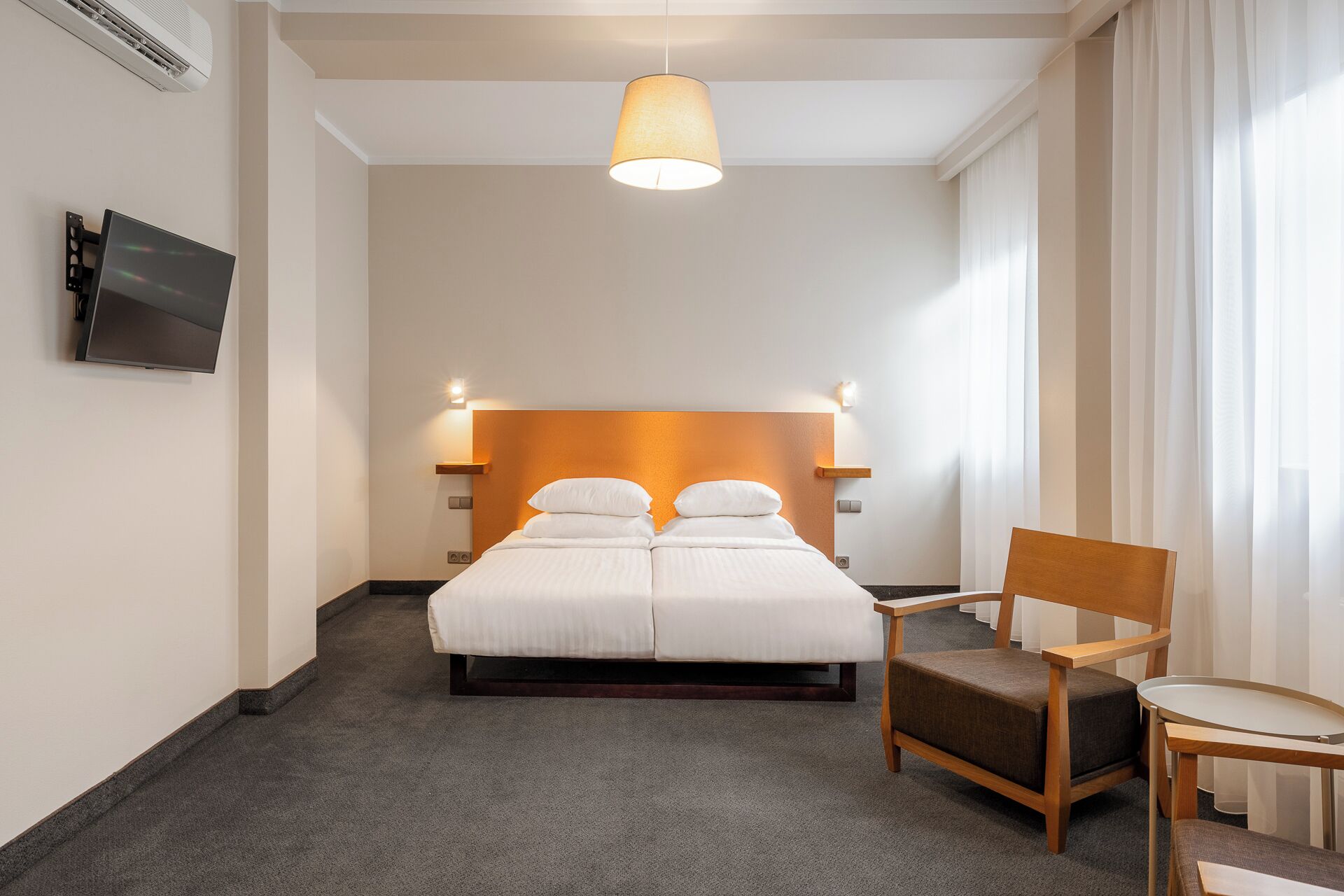 A hotel room with a large bed, a chair, a small table, and a TV mounted on the wall.