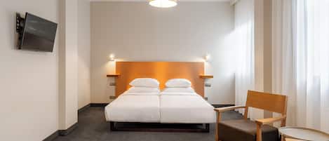 A hotel room with a large bed, a chair, a small table, and a TV mounted on the wall.