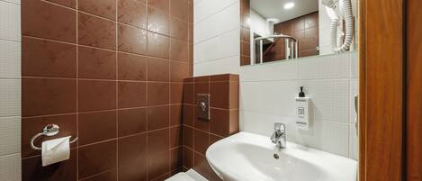 A bathroom with brown tiles, a white sink, a toilet, and a hairdryer.
