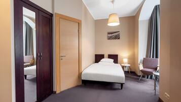 Una habitación de hotel con cama, mesitas de noche, una silla, armario y lámpara en el techo.