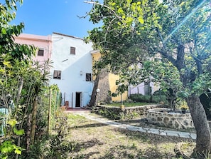 En innergård med en vit byggnad, en gång av sten och omgivande grönska.