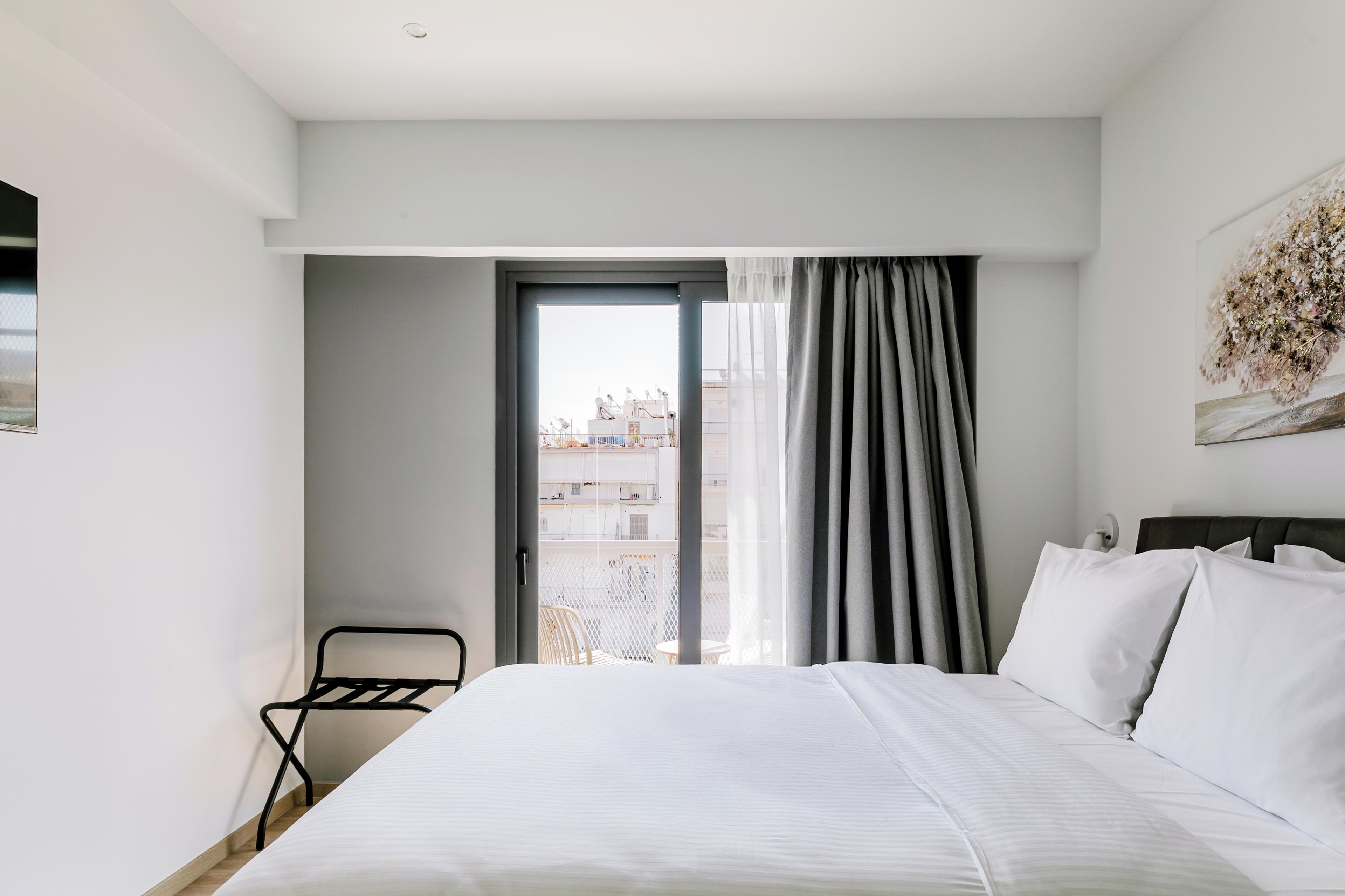 Habitación de hotel con cama, una silla, balcón con vista a edificios y ventana con cortinas.