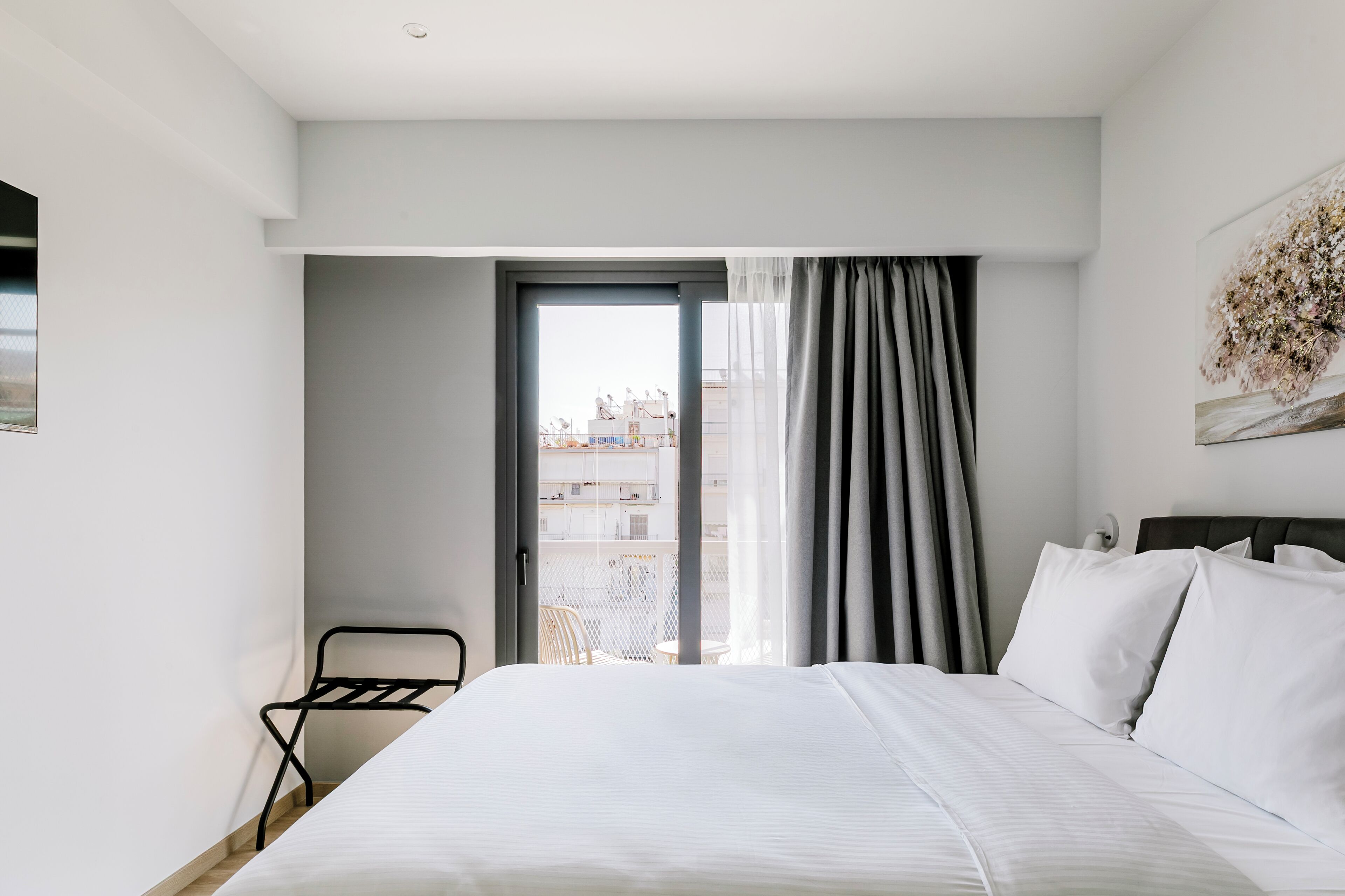 Una habitación de hotel moderna con una cama grande, una ventana con cortinas, una mesita pequeña y una silla.
