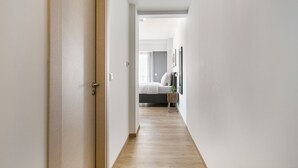 A narrow hallway with a wooden floor leading to a bedroom with a bed and a nightstand. - B48 Athens Dafni (Dafni-Ymittos)