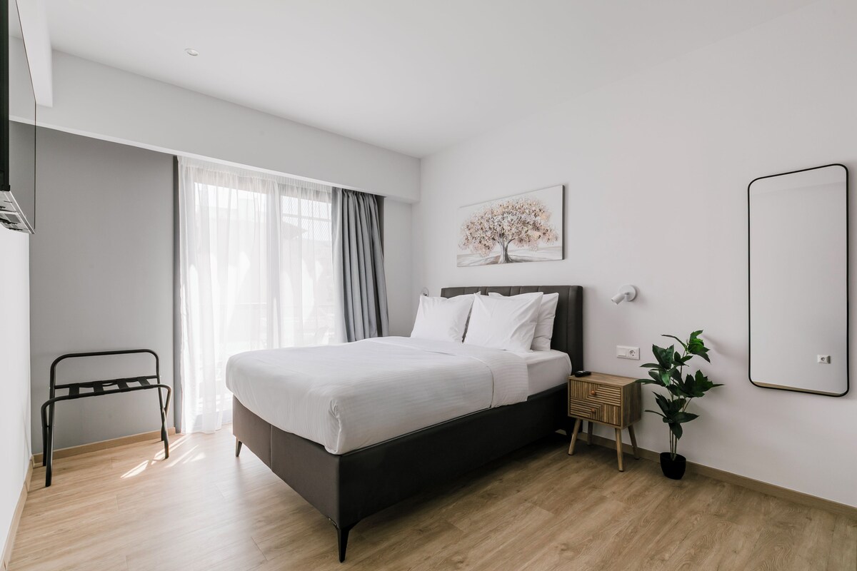 Une chambre d’hôtel moderne avec un grand lit, une table de chevet, un miroir et une fenêtre avec des rideaux.