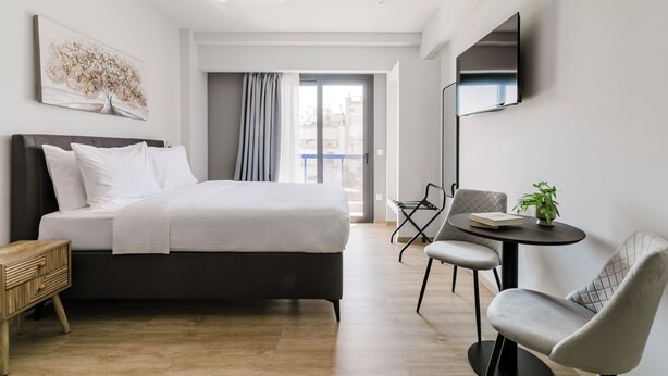 A modern hotel room with a bed, a desk, and a chair. There is a window with curtains, a flat-screen TV mounted on the wall, and a plant on the desk. - B48 Athens Dafni (Dafni-Ymittos)