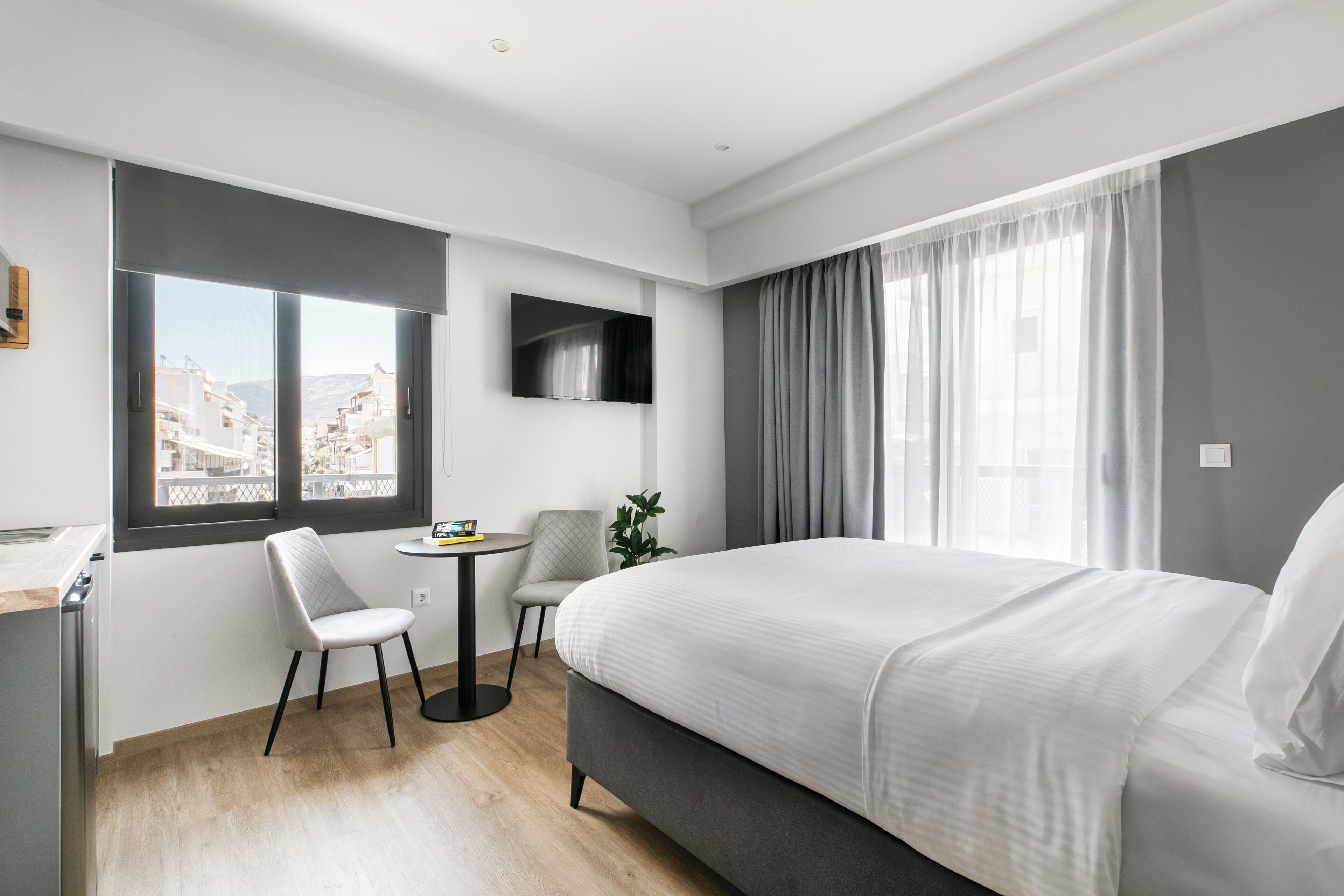 Een moderne hotelkamer met een groot bed, een bureau, een stoel, een kleine tafel en een aan de muur bevestigde televisie.