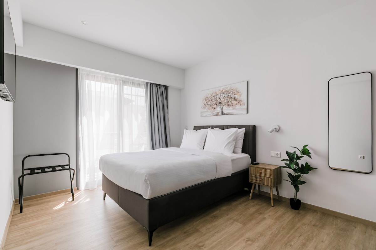 Una habitación de hotel moderna con una cama grande, una mesita de noche, un espejo y una ventana con cortinas.