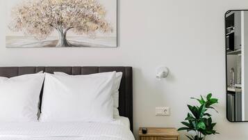 A bedroom with a bed, a bedside table, a wall-mounted light, a painting of a tree, and a potted plant.
