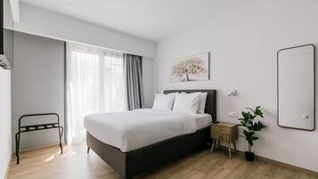 A modern hotel room with a large bed, a bedside table, a mirror, and a window with curtains.