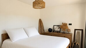 En pænt redt seng med hvide sengetæpper, et træhovedgærde og et sengebord med lampe og pynt.