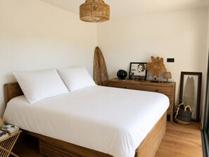 Un letto rifatto con lenzuola bianche, una testiera in legno e un comodino con una lampada e oggetti decorativi.