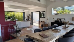 Et moderne køkken med en stor ø, et spiseområde med et tr æbord, og udsigt til grønne omgivelser.