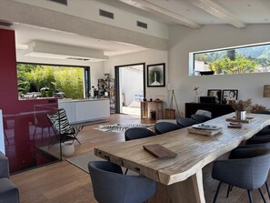Una cucina moderna con una grande isola, una zona pranzo con tavolo in legno e vista sul verde.