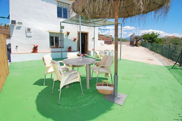 A patio with a round table and chairs, a hanging basket, and potted plants. - Cosy Poolside Escape for four - Salt-filtered pool. Breathtaking views. (COMARES)