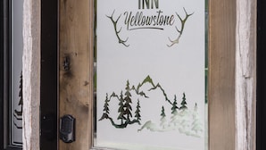 Eine Holztür mit einem Schild, auf dem "The Adventure Inn Yellowstone" steht, zeigt eine Silhouette von Bergen und Bäumen.