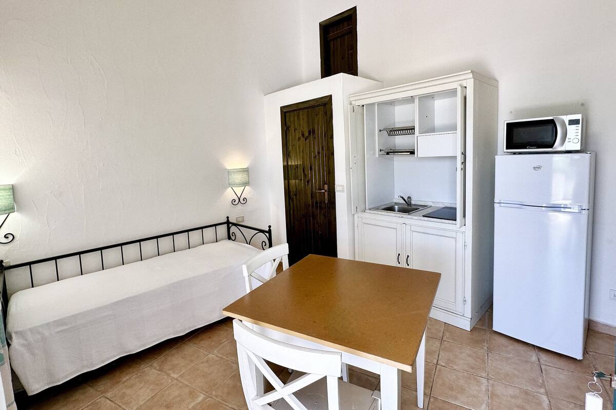 A compact kitchenette with a microwave, refrigerator, and a small dining area with a bench and table.