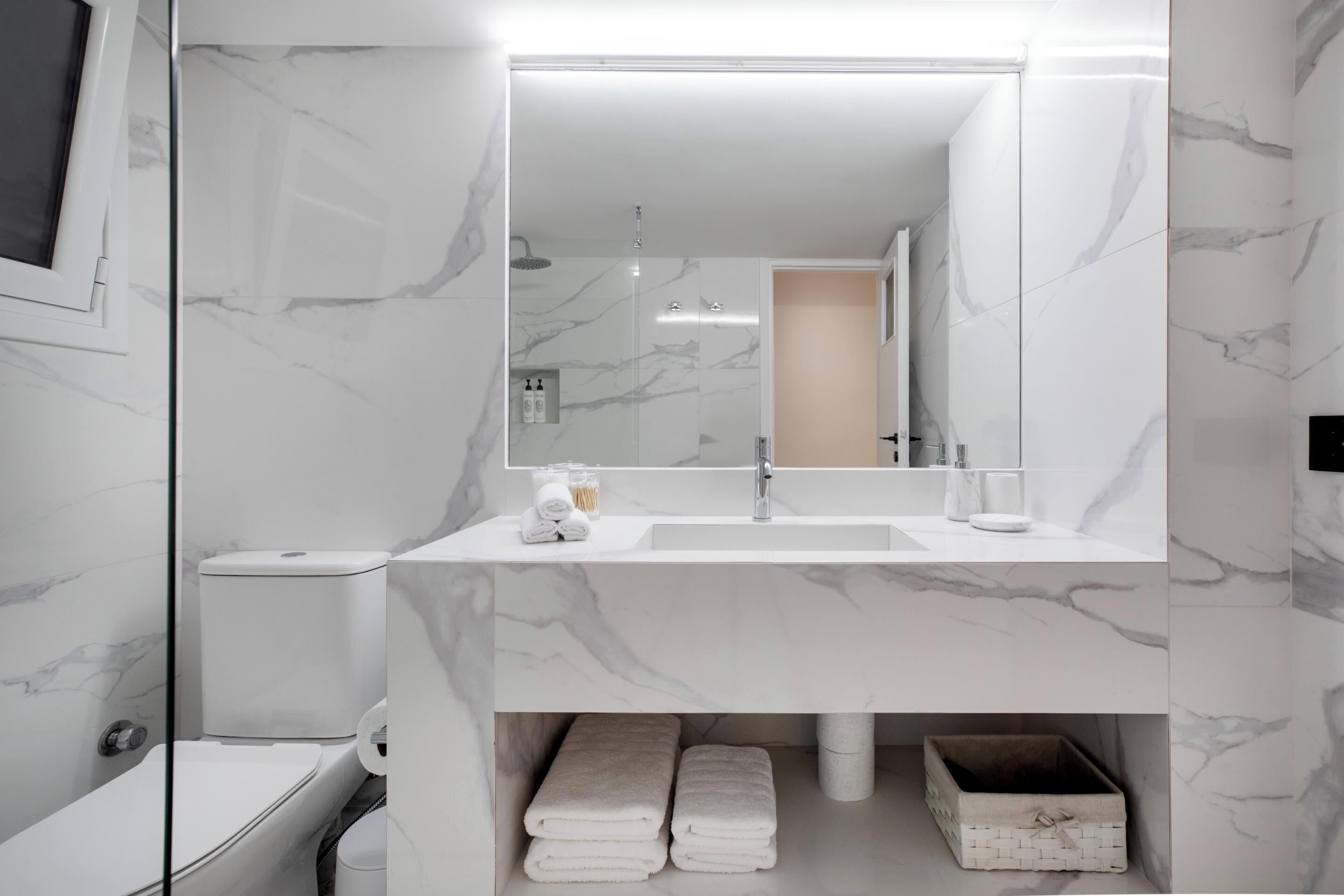 A modern bathroom with a white marble sink, a large mirror, and a glass-enclosed shower.