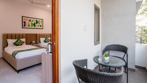 Habitación de hotel con una cama, una mesita con planta en maceta, ventilador de techo y ventana con vista a follaje.