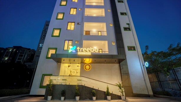 Un moderno edificio de hotel con un letrero destacado de 'treebo', varios pisos y una entrada acogedora con plantas en macetas.