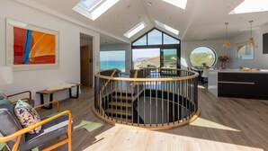 A spacious interior with a central spiral staircase, large windows offering views of the sea, and a modern kitchen area. - Ocean Skies - sleeps 10 guests  in 4 bedrooms (Porthtowan)