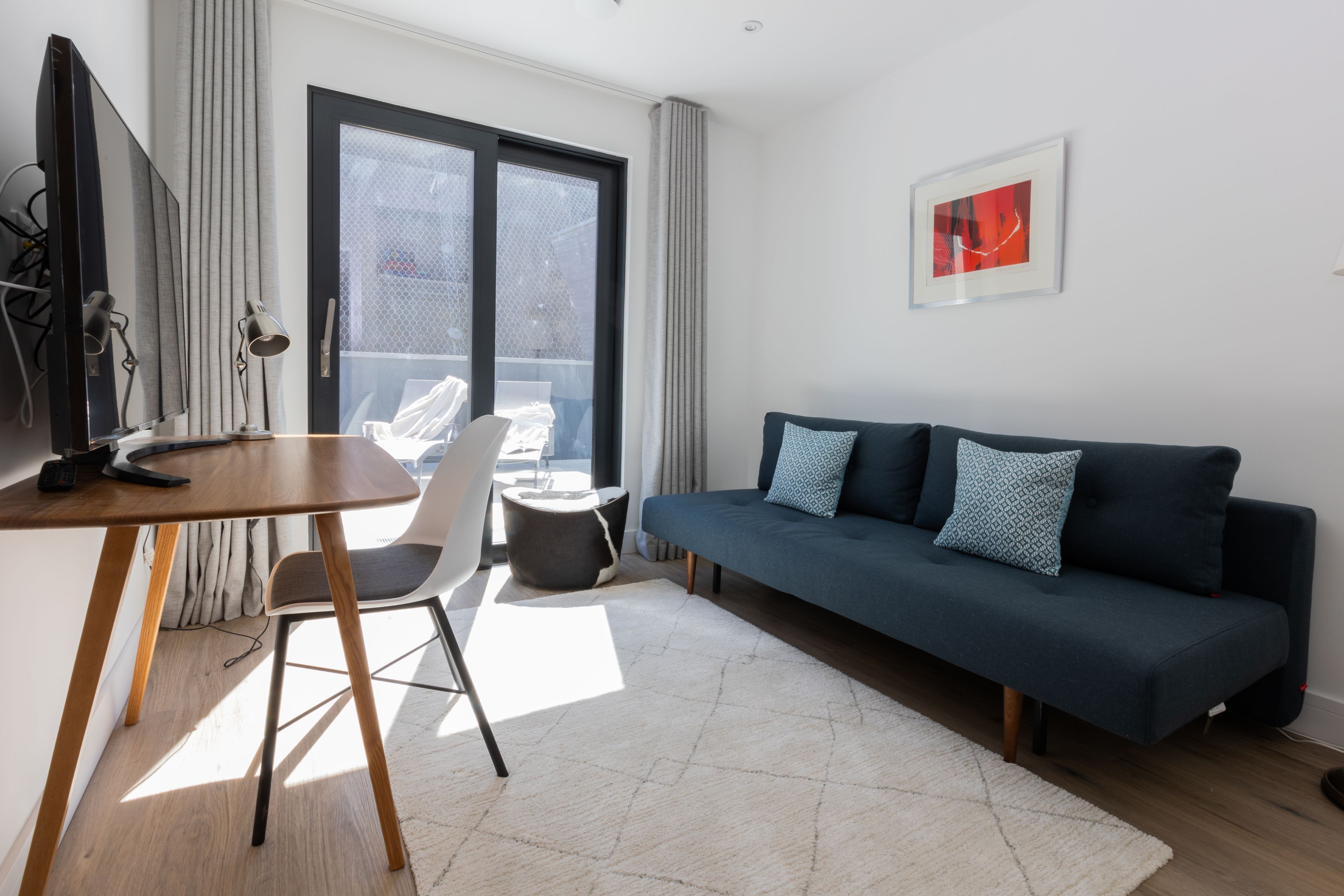 Un salon moderne avec un canapé bleu foncé, une table en bois, une chaise blanche et une grande fenêtre avec des rideaux.