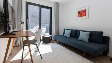 Un salon moderne avec un canapé bleu foncé, une table en bois, une chaise blanche et une grande fenêtre avec des rideaux.
