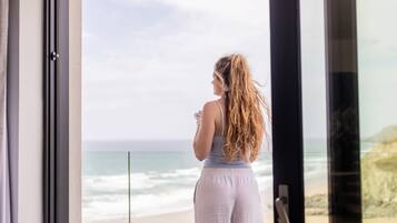 A person standing by a window overlooking a beach.