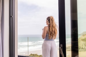 A person standing by a window overlooking a beach.