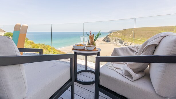 A balcony with a view of the sea, a table with food and drinks, and two chairs. - Ocean Skies - sleeps 10 guests  in 4 bedrooms (Porthtowan)