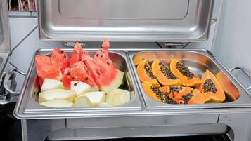 Un bufé de acero inoxidable con dos secciones: una con sandía y manzanas, y la otra con papaya y piña.