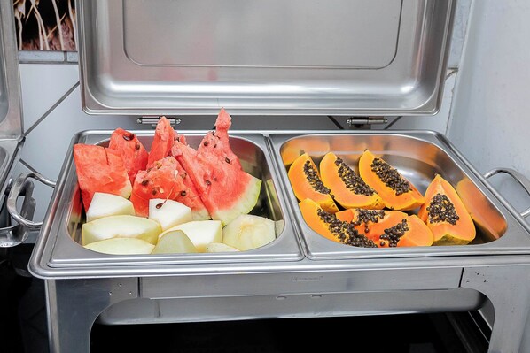 A stainless steel buffet with two sections: one with watermelon and apples, and the other with papaya and pineapple.