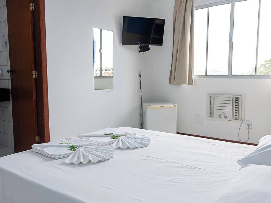 Una habitación de hotel con una cama, un televisor montado en la pared, una ventana con cortinas y un radiador.