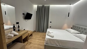 Un dormitorio moderno con cama, mesitas de noche, espejo, televisor y ventana con cortinas.