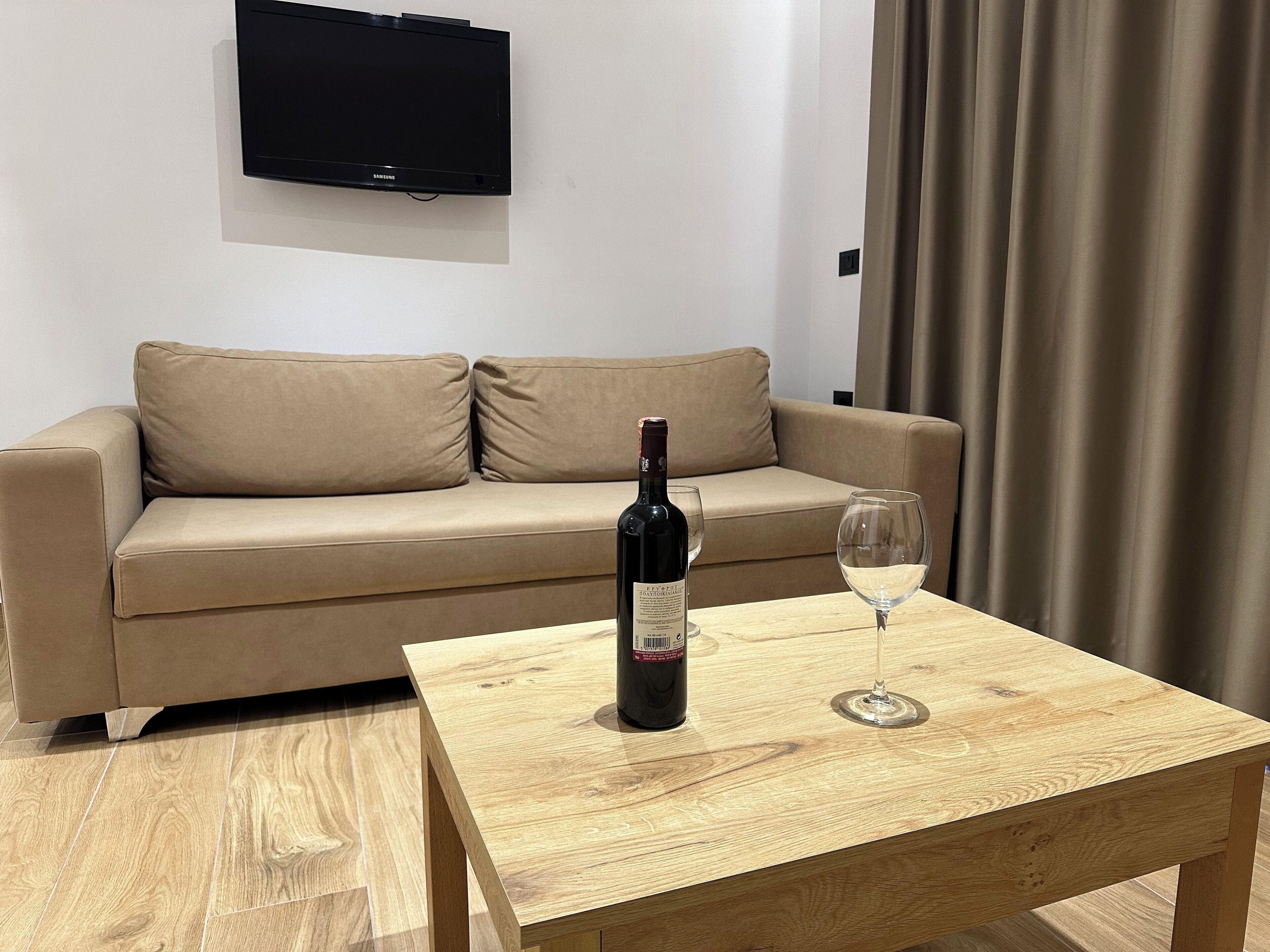 A modern living room with a beige sofa, a wooden coffee table, a bottle of wine, and an empty wine glass.